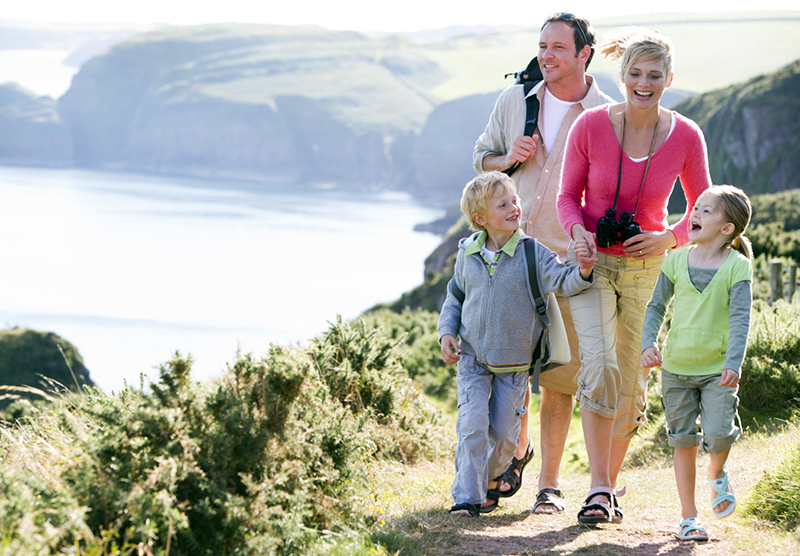 Family walking on cliffside path holding hands and smiling